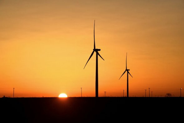 2019年2月12日，美國德克薩斯州大斯普林的二疊紀盆地石油和天然氣生產區，風力渦輪機在日出時運行。